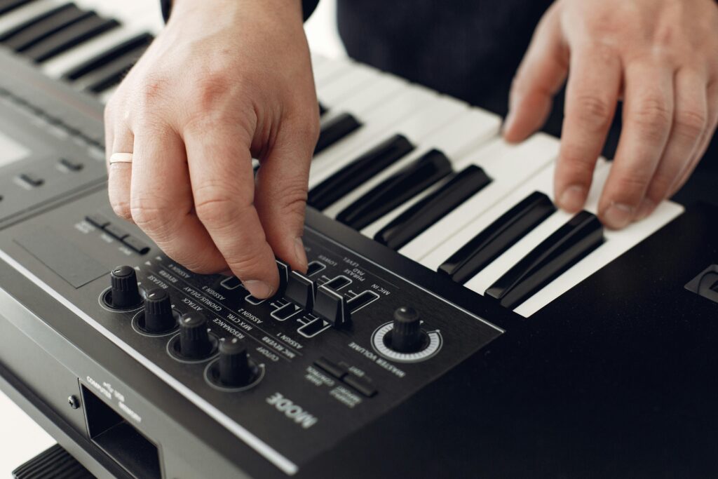 Close-up of hands adjusting synthesizer controls with piano keys in view.
